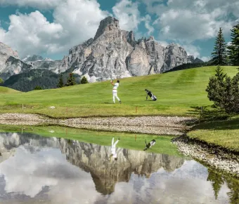 Man golfing in the Dolomites, reflected in a serene mountain lake